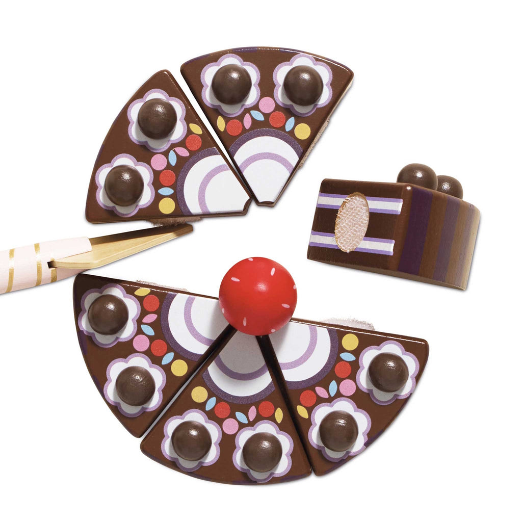 Wooden toy cake sliced into six pieces, decorated with chocolate balls and a red strawberry on top. A pink-striped plastic knife is inserted. Playful and colorful.