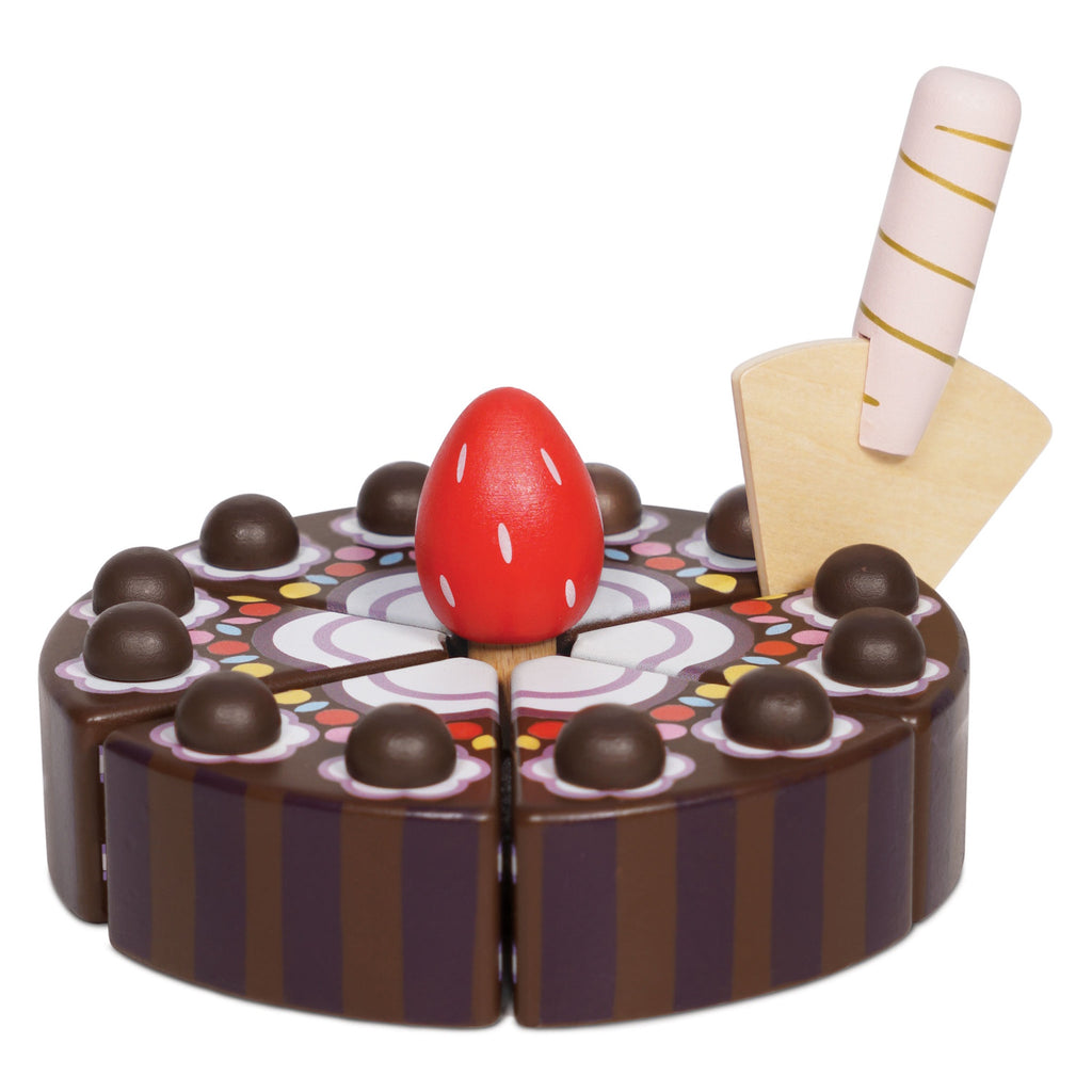 Wooden toy cake sliced into six pieces, decorated with chocolate balls and a red strawberry on top. A pink-striped plastic knife is inserted. Playful and colorful.