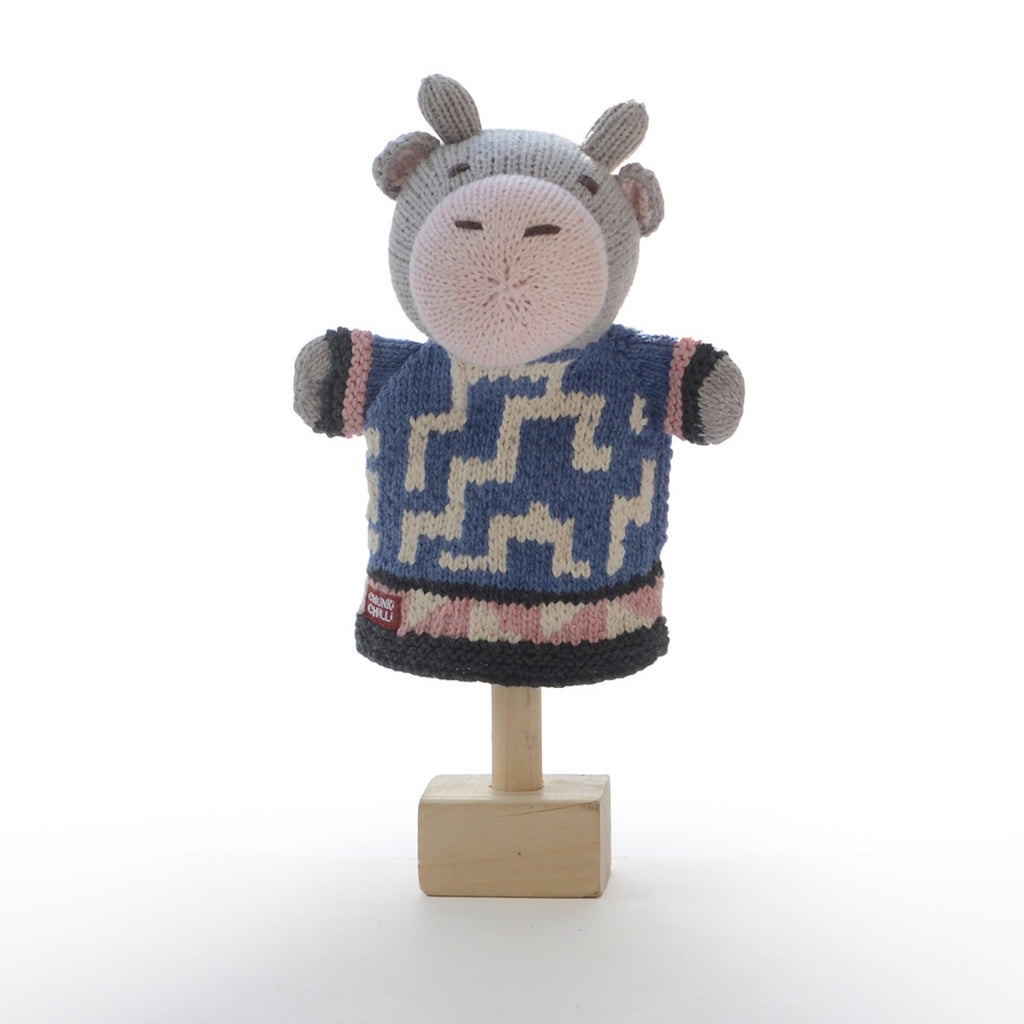 Knitted hand puppet of a gray cow with beige snout and ears, wearing a blue and cream zigzag-patterned sweater. It conveys a playful, whimsical tone.