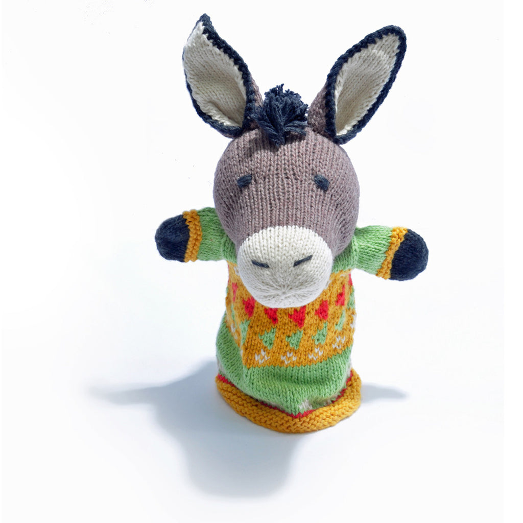 A knitted donkey puppet with a friendly face wears a colorful sweater with orange, yellow, and green patterns. Its ears are perked up, conveying a playful tone.