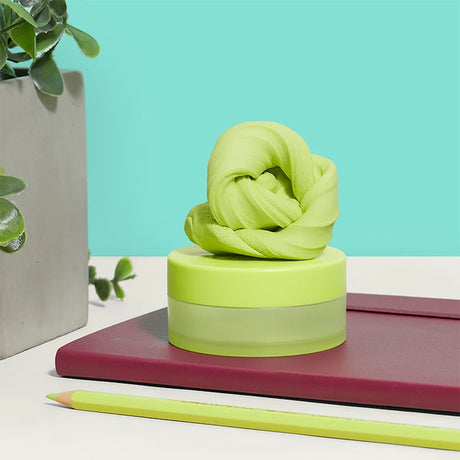 Light-green focus putty on its container, resting on a burgundy notebook next to a pencil and plant.