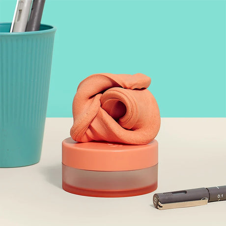 Orange thinking putty twisted into a swirl atop its small container on a desk next to pens.
