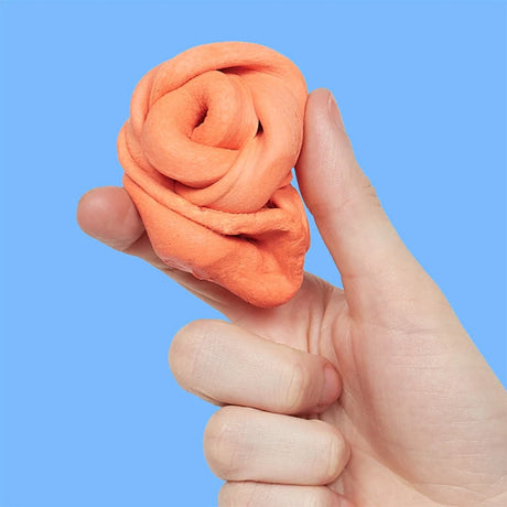 Hand holding a folded mound of clementine-orange focus putty against a bright blue background.