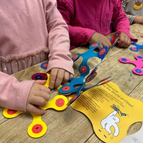Children playing with colorful, flexible magnetic Clixo toy pieces on a wooden table.