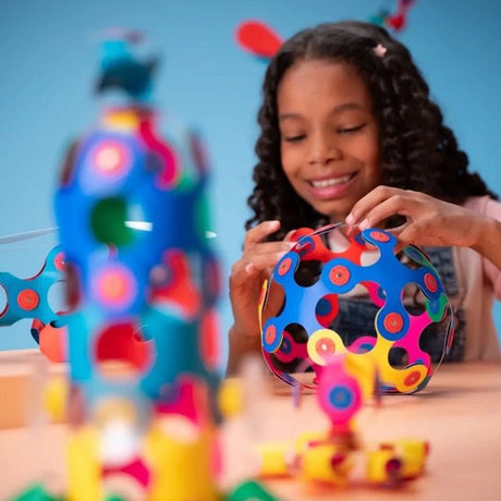Young girl smiling while building a colorful geometric sphere using flexible magnetic toy pieces.