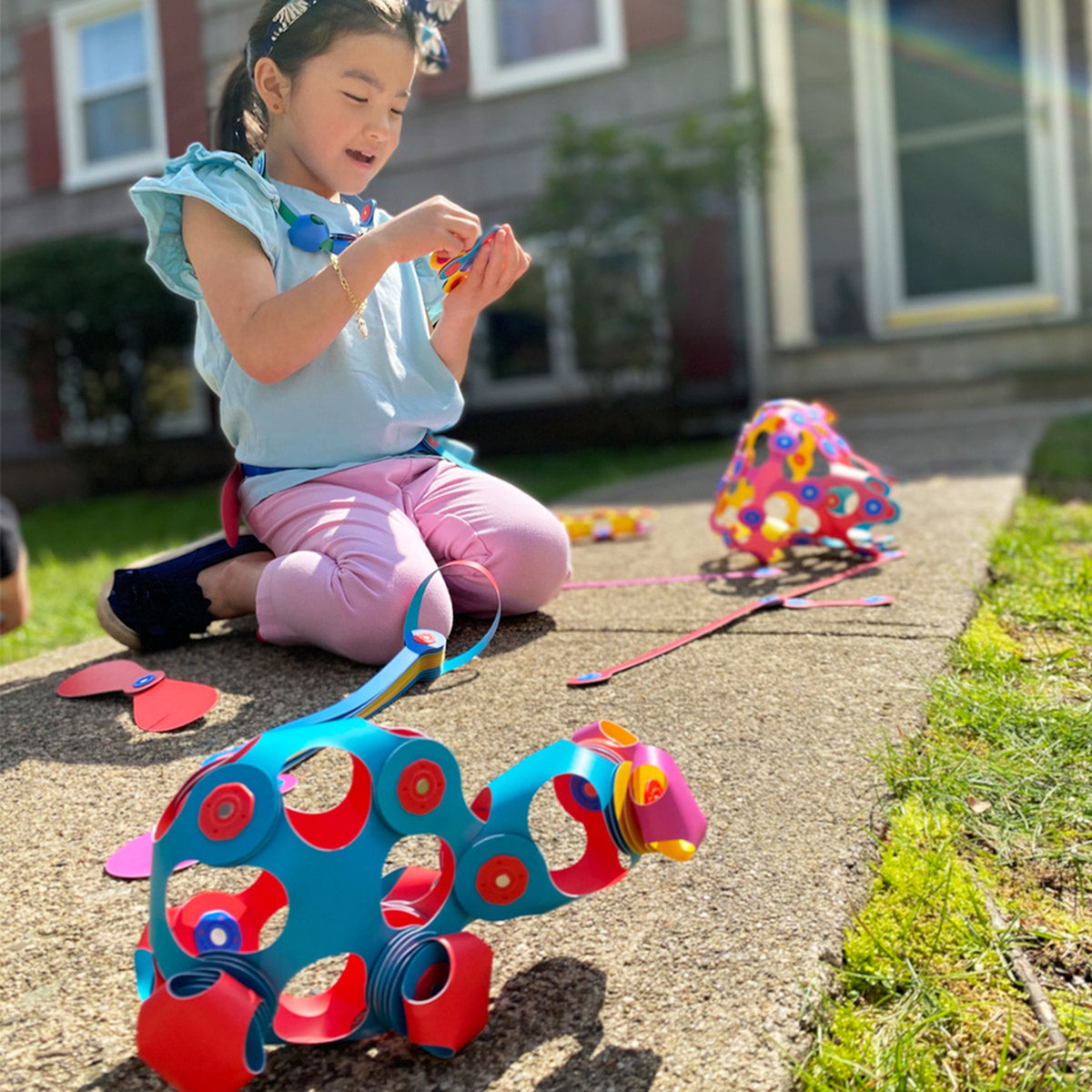 Young girl sitting outside on a walkway playing with colorful flexible magnetic toy pieces and creations.