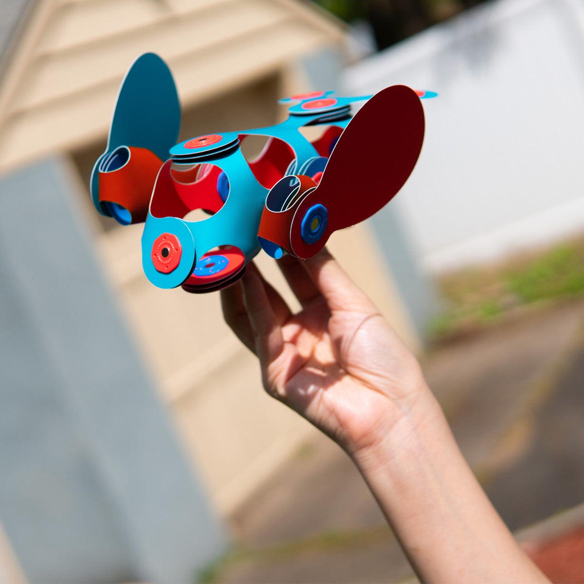 A hand holding a colorful turquoise and red magnetic toy creation shaped like a flying creature outdoors.