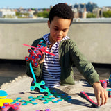 Young boy playing outdoors on a wooden table with colorful magnetic Clixo building pieces and a toy creation.