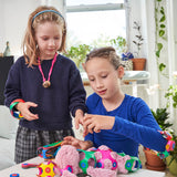 Two young girls sitting at a table together, playing and dressing up a pink stuffed toy using Clixo pieces.