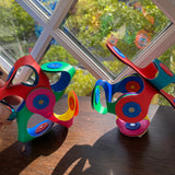 Two colorful, flexible magnetic building creations sitting on a wooden windowsill in sunlight.
