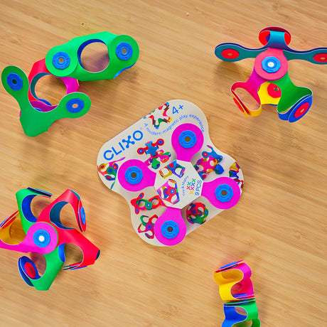 Colorful Clixo Tiny & Mighty 9-piece magnetic building set surrounded by folded 3D shapes on a wooden surface.