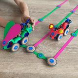 Child playing with colorful magnetic Clixo vehicles and wooden wheels along flexible pink and green tracks.