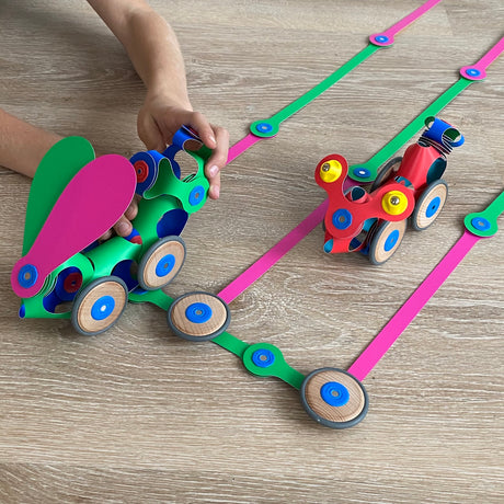Child playing with colorful magnetic Clixo vehicles and wooden wheels along flexible pink and green tracks.