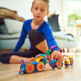 A child playing on the floor with colorful toy vehicles built from flexible magnetic pieces and wooden wheels.