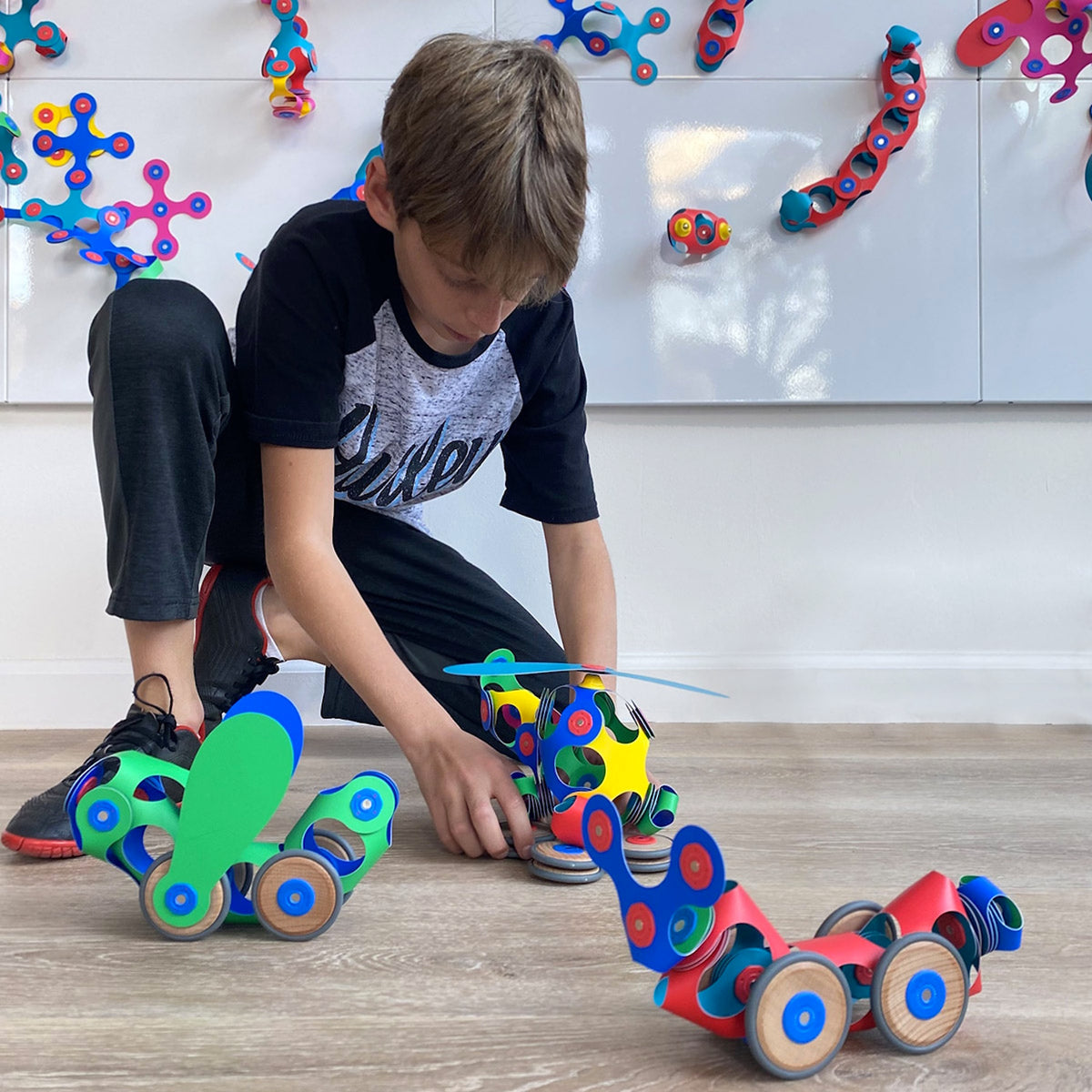 Boy playing on floor with colorful magnetic toy vehicles made with the Clixo Wheel Creator Pack.