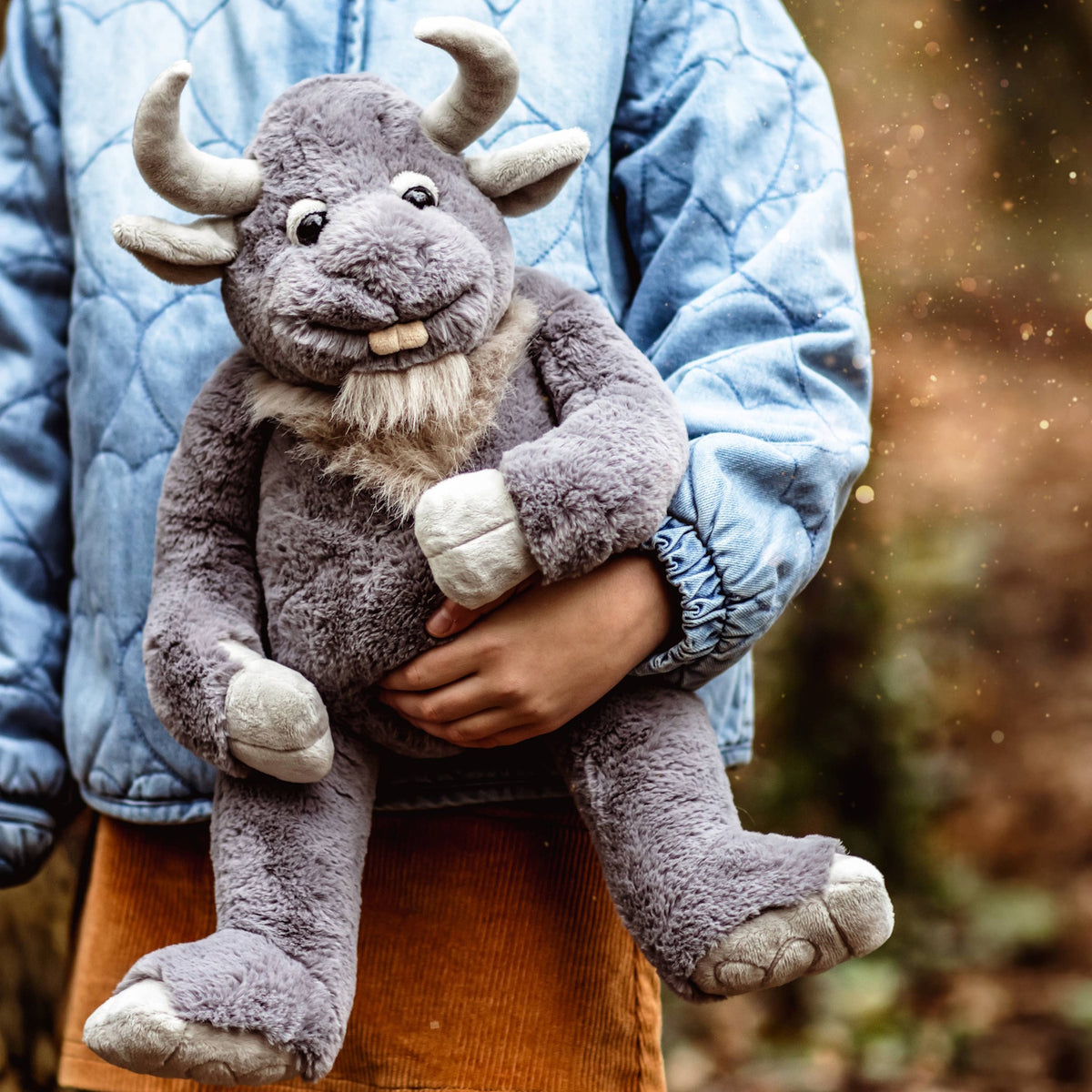 A person in a blue jacket holding a plush grey horned creature toy outdoors.