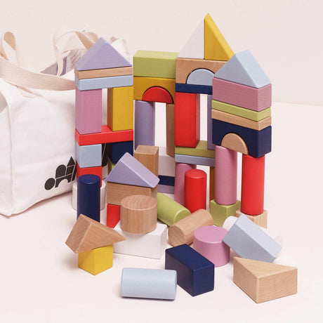 Colorful wooden building blocks in various geometric shapes with a white canvas storage bag.