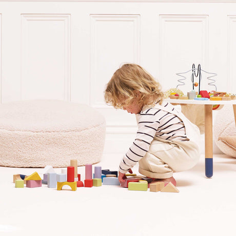 Child crouching on floor playing with colorful wooden building blocks in a modern room setup.