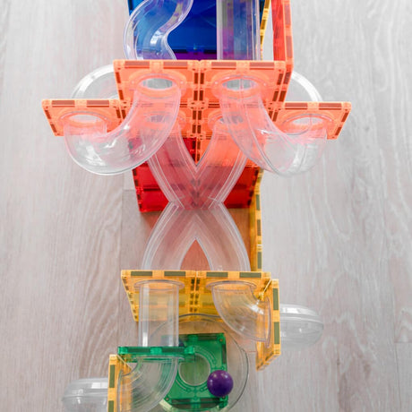 Top-down view of a colorful magnetic tile ball run structure with clear tubes on a light wooden floor.