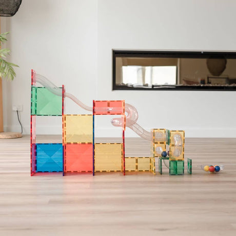 Colorful magnetic tile ball run structure with clear chutes set up on a wooden floor in a living room.