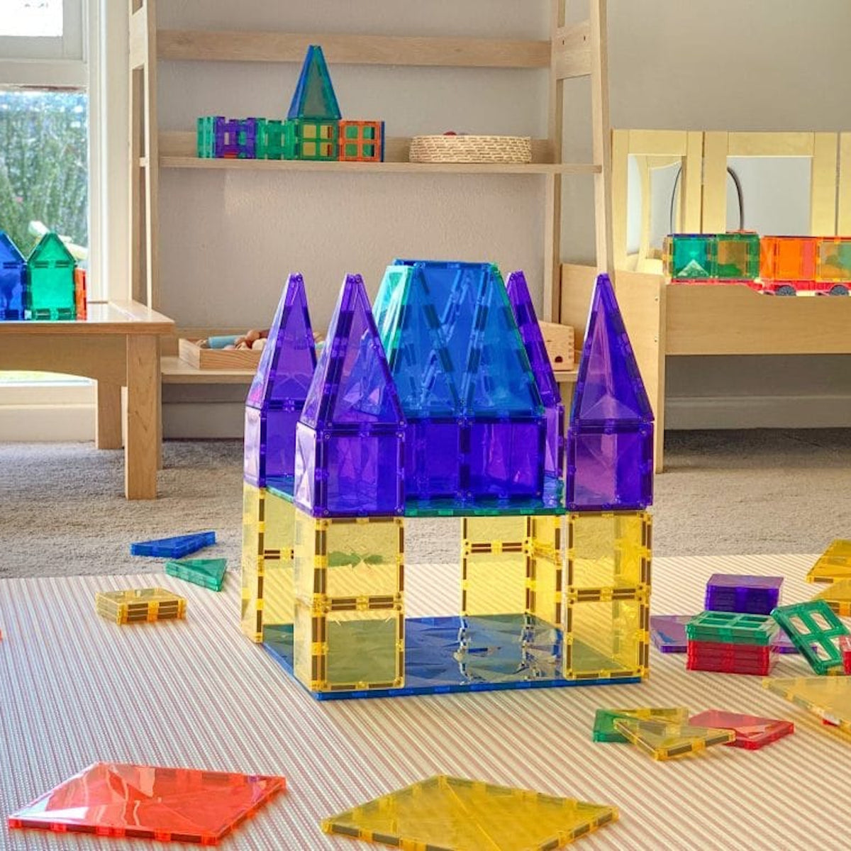 Colorful toy castle built with magnetic tiles on a play mat in a sunlit playroom.