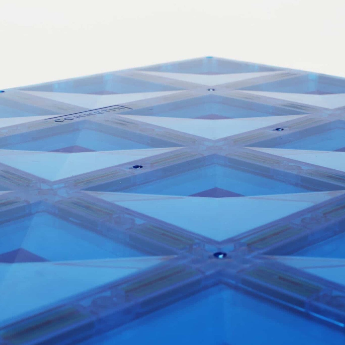 Close-up of a translucent blue magnetic tile base plate with a faceted geometric pattern and rivets.