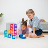 Two young children playing with a magnetic tile ball run structure on a white rug.