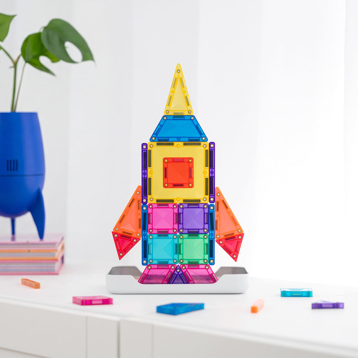 Colorful toy rocket ship built from magnetic building tiles on a white surface.