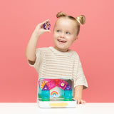 Young girl holding up a magnetic tile, playing with a magnetic set built inside a metal travel case.
