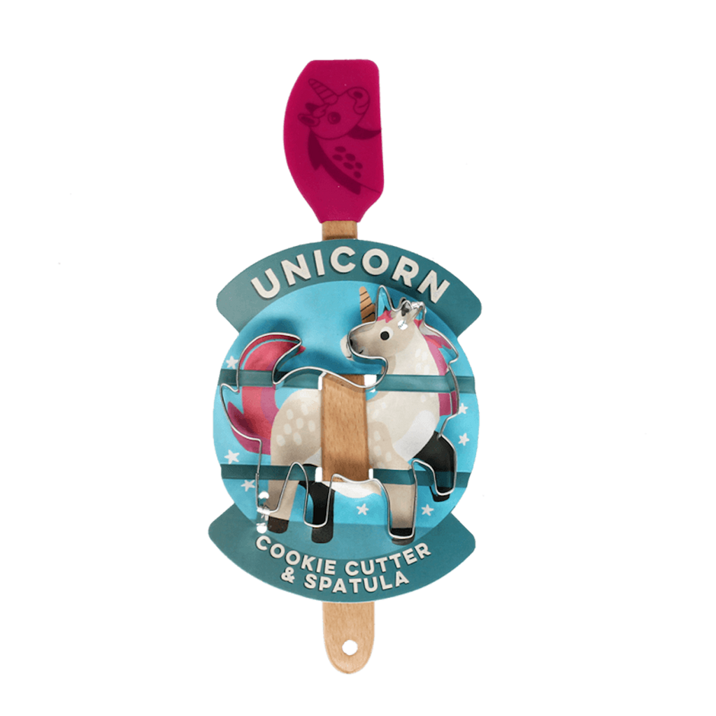 A pink spatula with a unicorn image lies next to a silver unicorn-shaped cookie cutter. The wooden handle adds a whimsical touch.