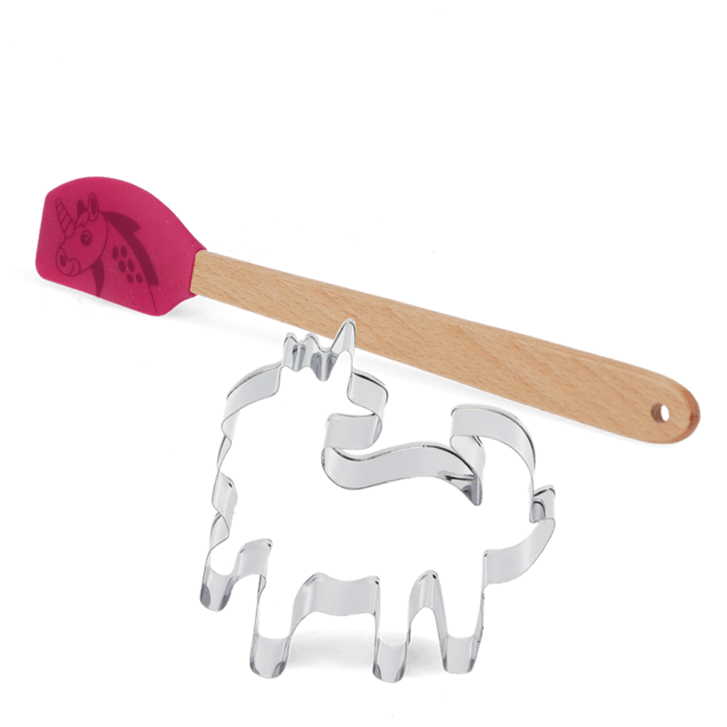 A pink spatula with a unicorn image lies next to a silver unicorn-shaped cookie cutter. The wooden handle adds a whimsical touch.