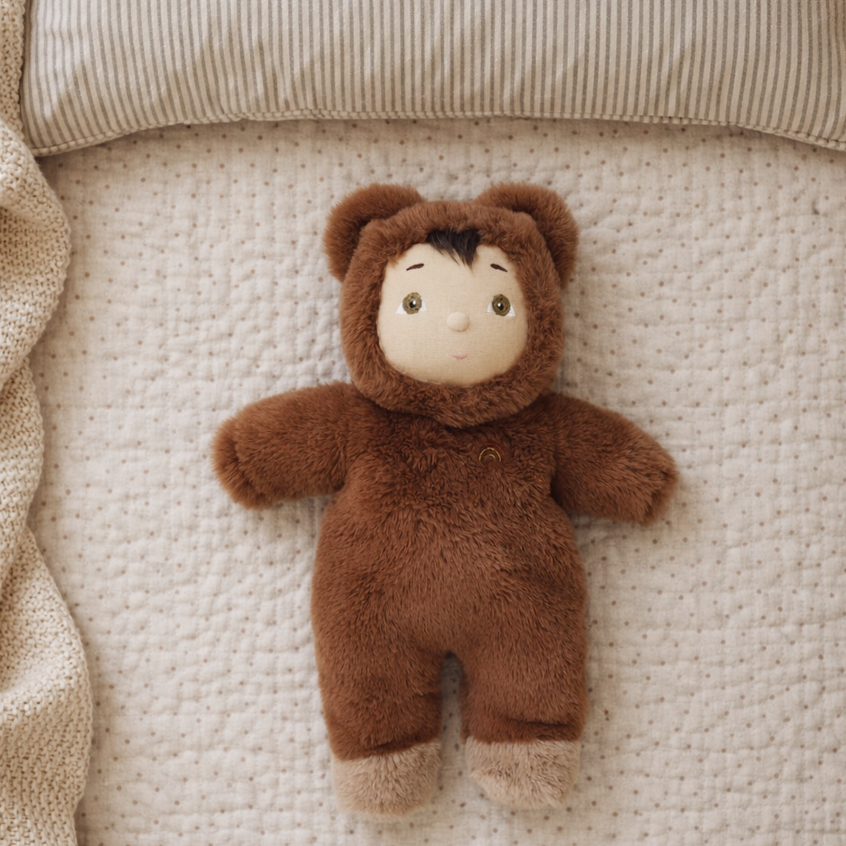 Cozy Day Dinkum Bobby Bear doll lying on a soft, polka dot quilted blanket.