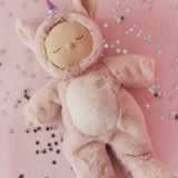 Olli Ella Cozy Dinkum Unicorn Sugarpie plush doll lying on a pink background with star confetti.