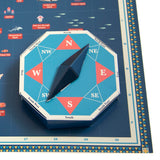 3D papercraft compass spinner resting on an illustrated blue map with cardinal directions.