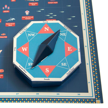 3D papercraft compass spinner resting on an illustrated blue map with cardinal directions.