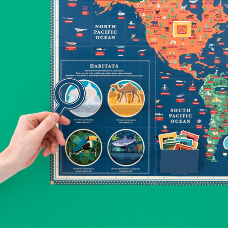 Hand holding a paper magnifying glass over an illustrated animal kingdom map with habitat pop-ups.