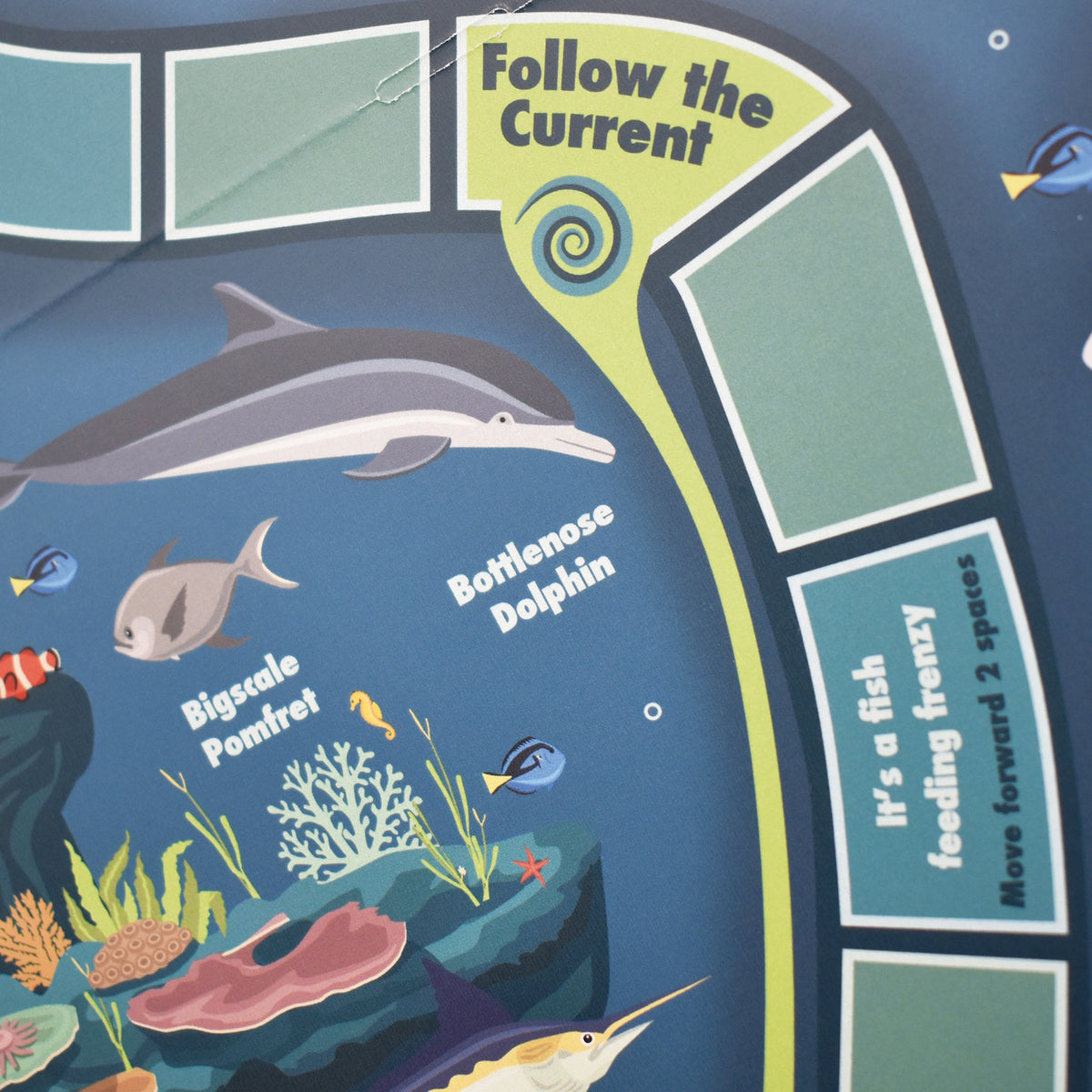 Detail of an ocean board game featuring a dolphin, coral, and a "Follow the Current" game track.