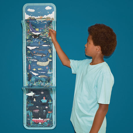Young boy pointing at a vertical ocean layer activity craft hanging against a blue background.