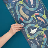 Hand placing a game piece on a ocean-themed board game with sea creatures and underwater facts.