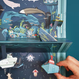 Detailed 3D pop-up seascape featuring marine creatures, a sunken ship, and a hand holding a paper submarine toy.