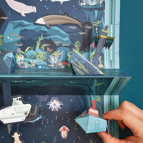 Detailed 3D pop-up seascape featuring marine creatures, a sunken ship, and a hand holding a paper submarine toy.