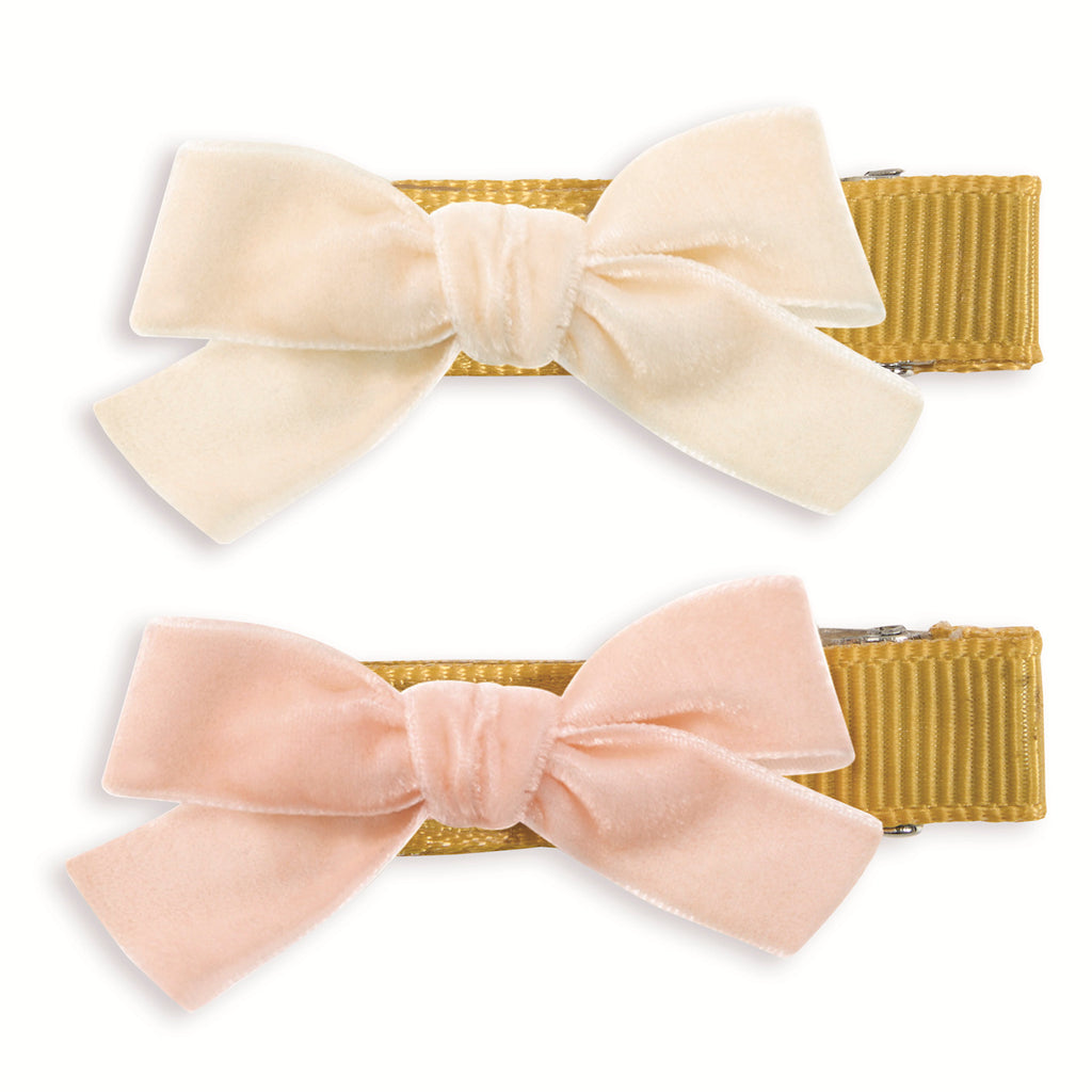 Two velvet bow clips on golden alligator clips; the top bow is ivory, and the bottom is pale pink. The tone is soft and elegant.
