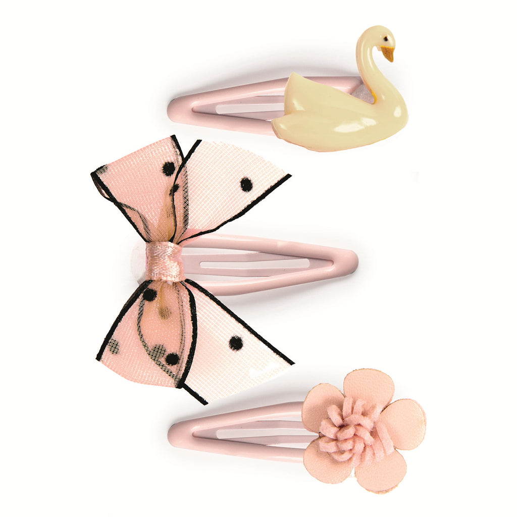 Three pastel pink hair clips are arranged vertically on a white background, a swan, a polka-dot bow, and a flower. The tone is playful and feminine.
