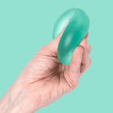 A hand squeezing and deforming a squishy, teal-green Speks stress toy against a mint background.
