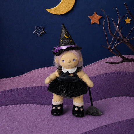 Plush doll with purple hair in a black witch dress and pointed hat, standing next to a toy broom.