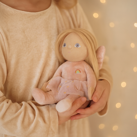 Child holding a blonde plush fairy doll with wings and a rainbow dress.