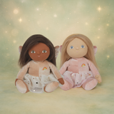 Two Olli Ella Dinky Dinkum fairy dolls with wings sitting together against a sparkling green background.
