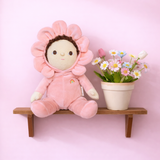 Olli Ella Dinky Dinkum Dahlia flower doll sitting on a wooden shelf next to potted daisies.