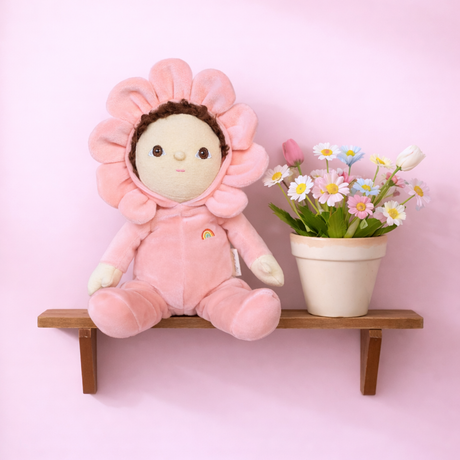 Olli Ella Dinky Dinkum Dahlia flower doll sitting on a wooden shelf next to potted daisies.