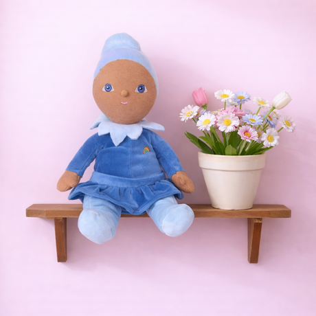 Olli Ella Dinky Dinkums Iris doll sitting on a wooden shelf next to a pot of daisies.